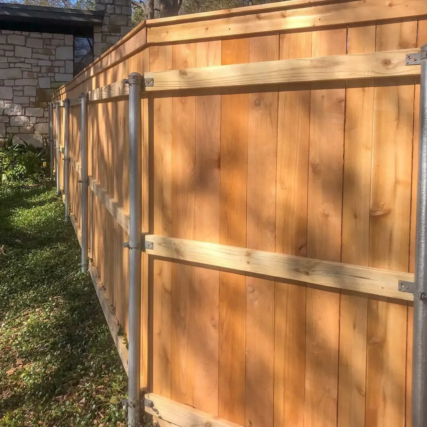 Wooden fence with vertical planks and horizontal rails, supported by metal posts in a grassy area.