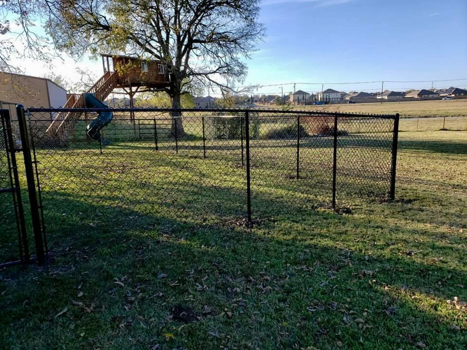 Black chain-link fence in grassy backyard, a playground with a slide in the background.