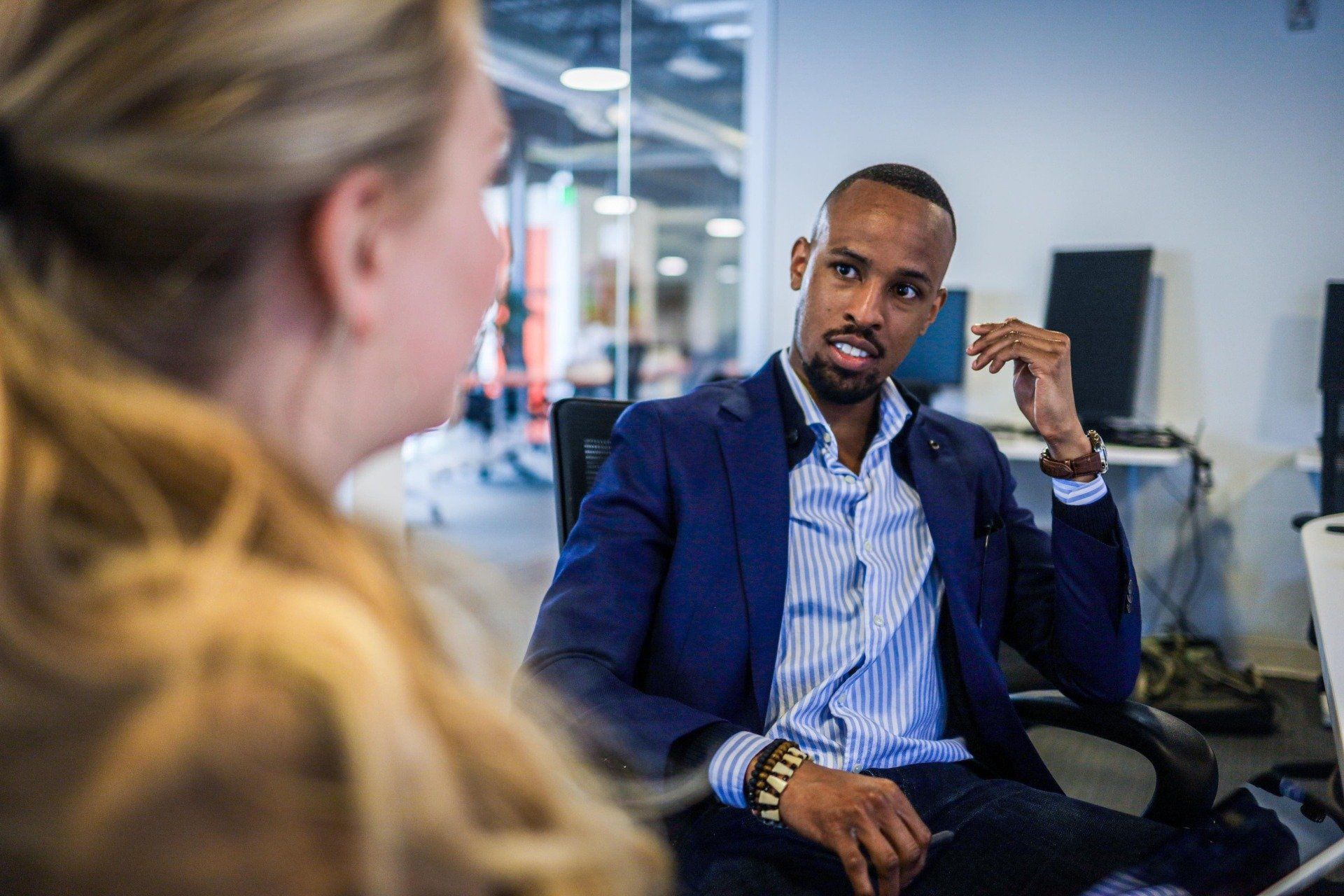 A man in a suit is sitting in a chair talking to a woman.