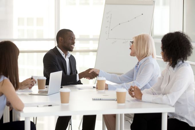 A group of people are sitting around a table shaking hands.