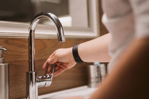 Hand turning on a kitchen faucet over a sink, with water running.