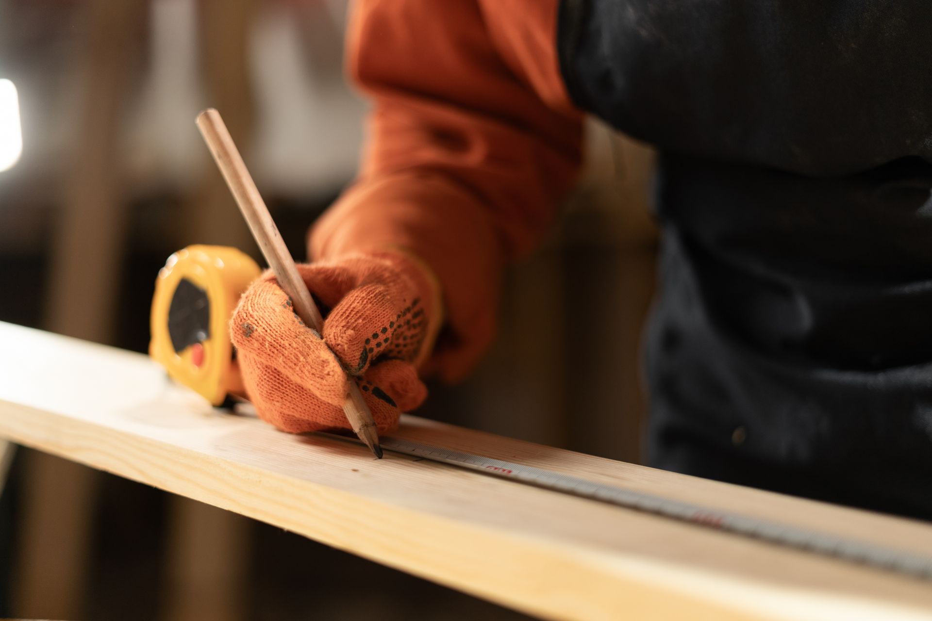Gloved hands measuring a wooden plank with a ruler on a workbench