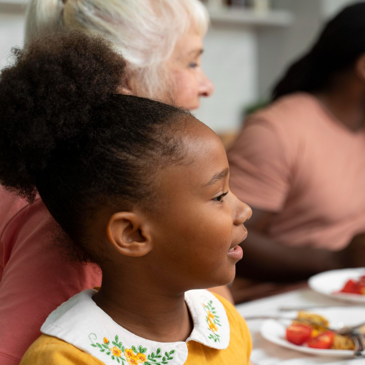 Child in a classroom eating at a table, with other people seated nearby