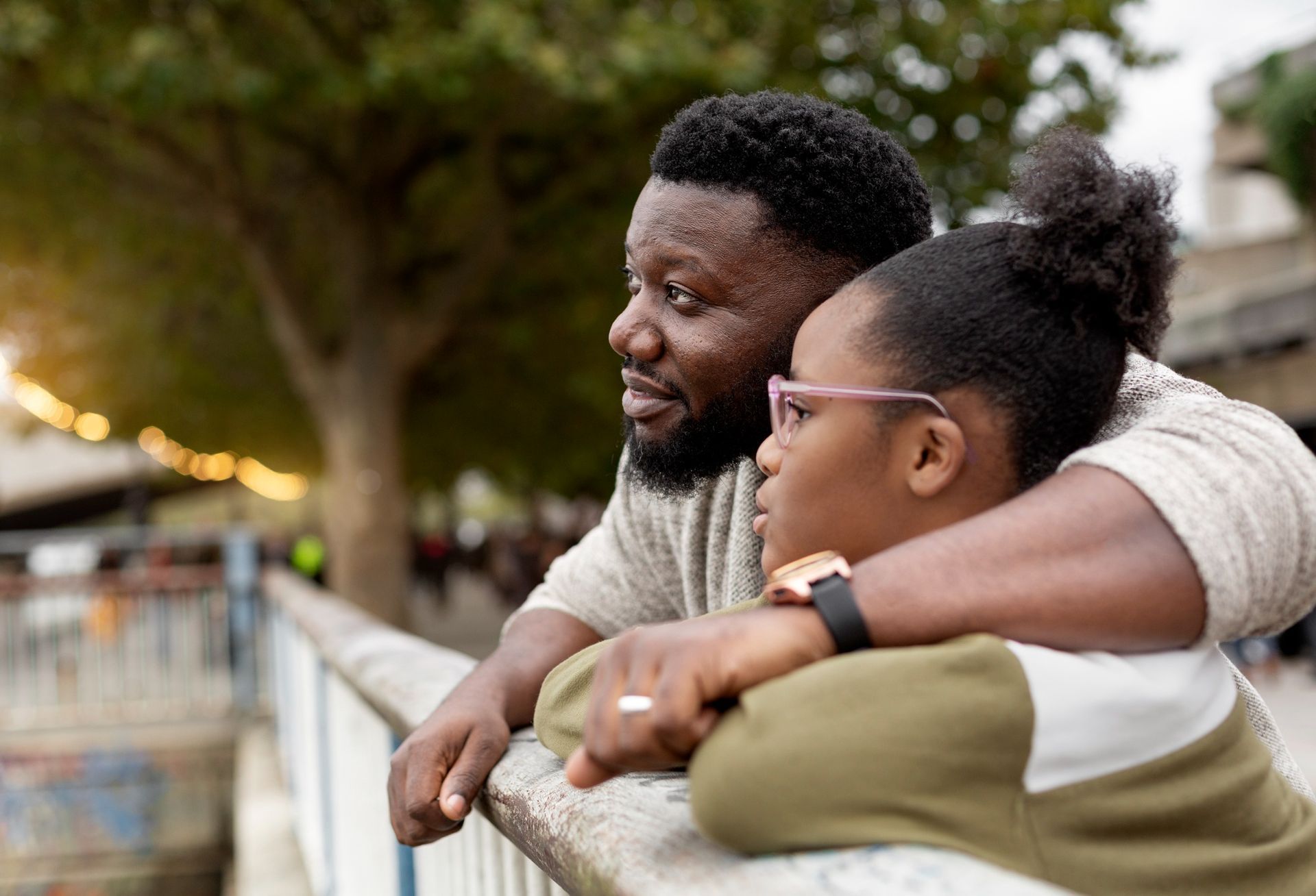 Two people leaning on a railing, smiling and looking out over a tree-lined waterfront at dusk