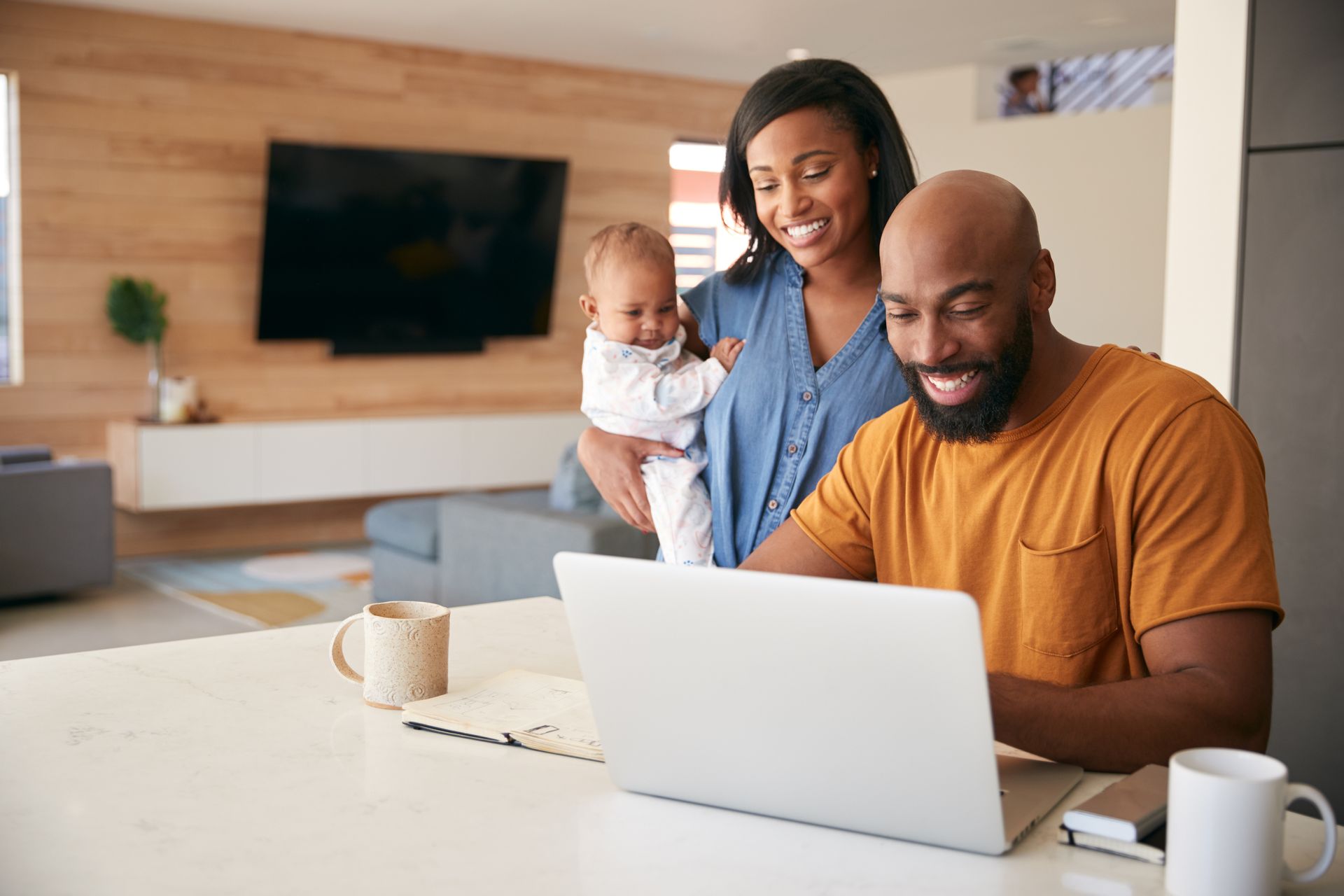 Family smiling around a laptop at a dining table in a bright living room