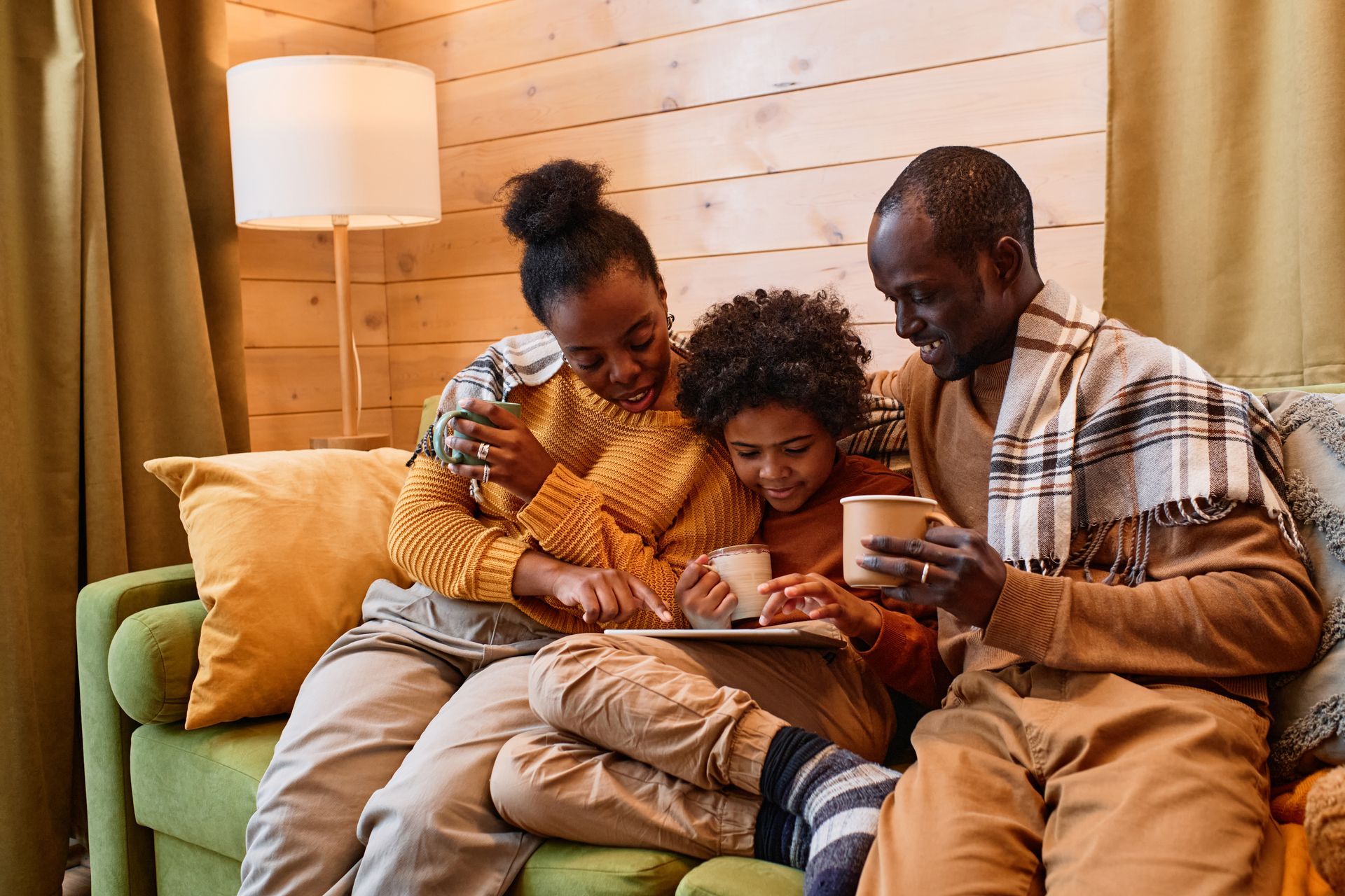 Three people sitting on a couch, smiling and looking at a tablet in a cozy living room.