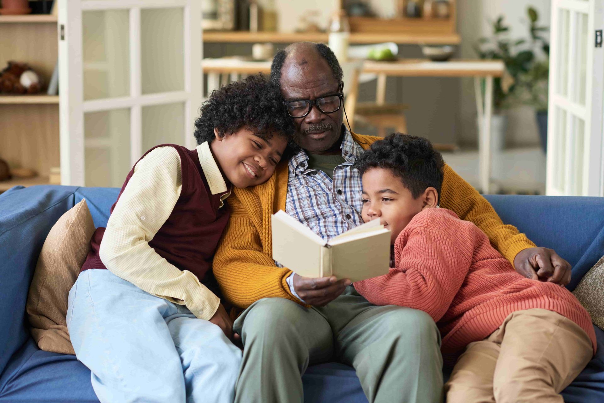 Three people sitting on a couch reading a book together in a bright living room