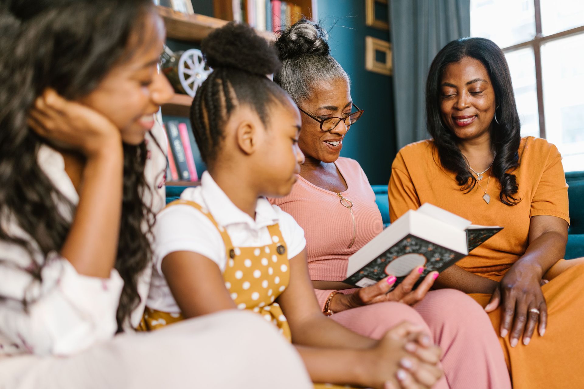 Four people sit on a couch, reading a book together in a cozy living room.