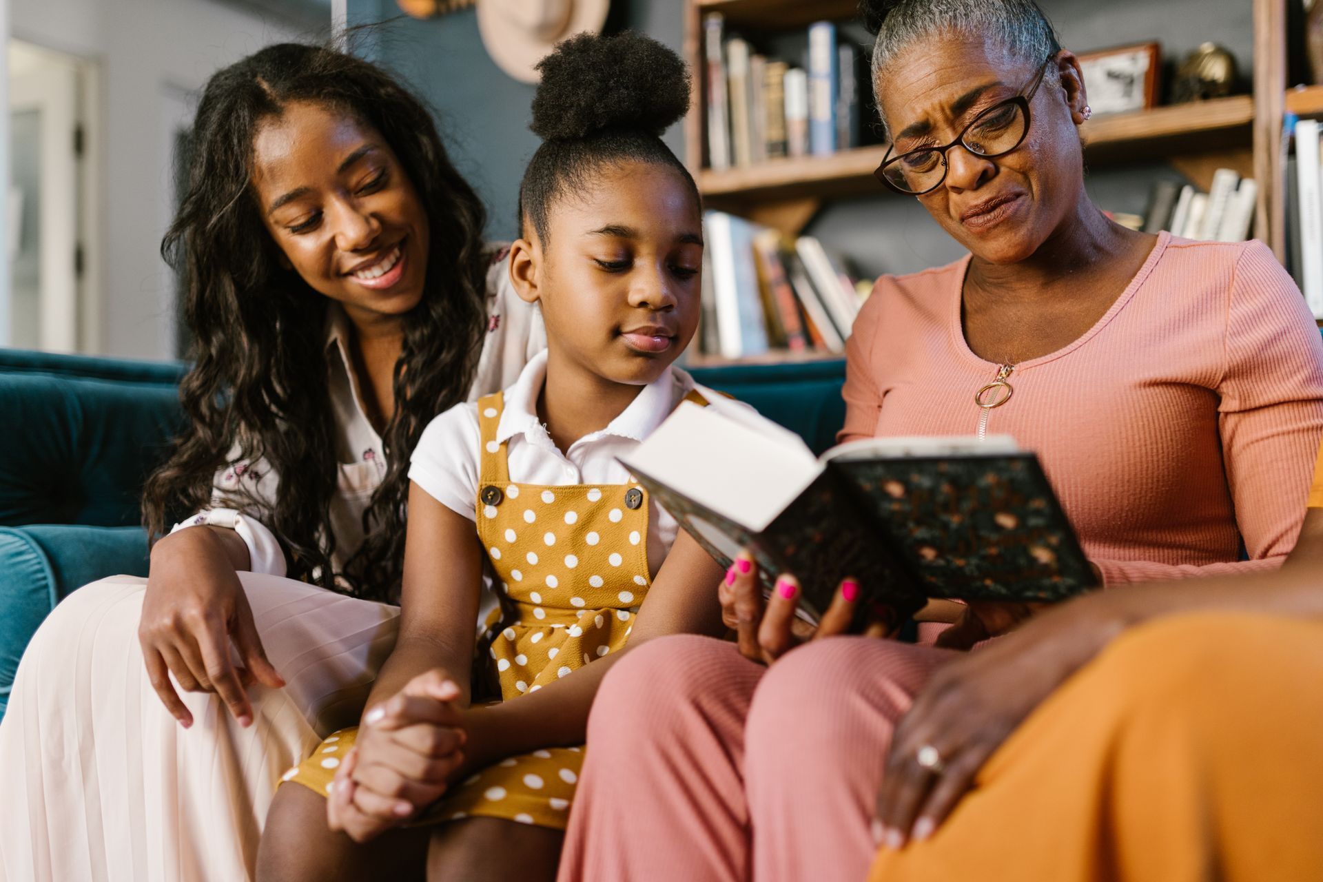 Three people sitting on a couch, reading a book together in a cozy living room.