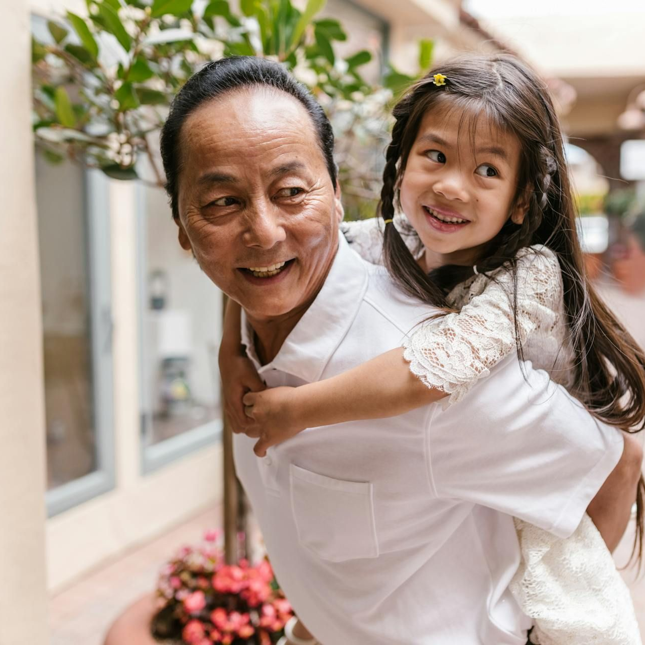 Smiling man giving a piggyback ride to a laughing child in a bright garden walkway