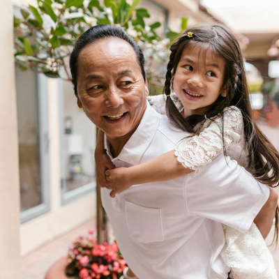 Smiling child riding on an adult’s back in a bright indoor corridor with plants and flowers