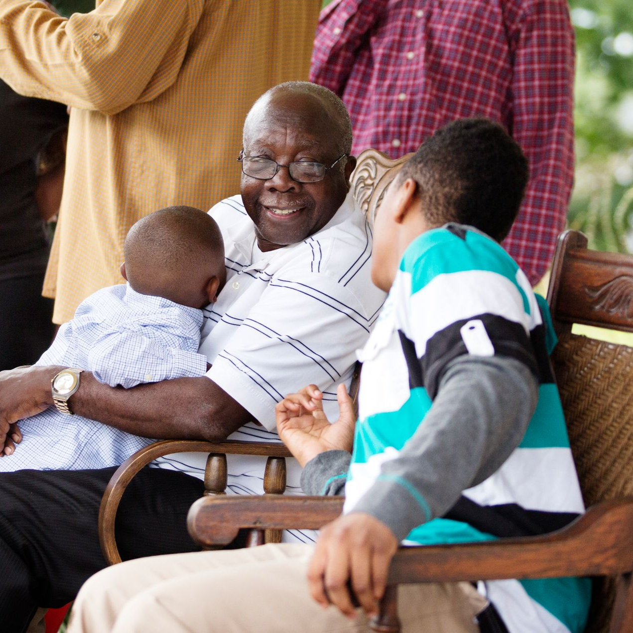 Older man holding a sleeping baby while seated with children on a wooden bench outdoors