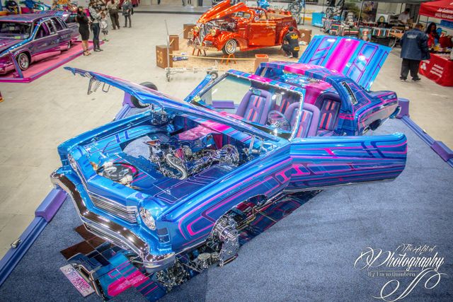 Bright blue-and-pink lowrider car with hood open at an indoor car show