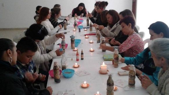 Personas sentadas en una mesa haciendo manualidades, velas encendidas, materiales de arte.