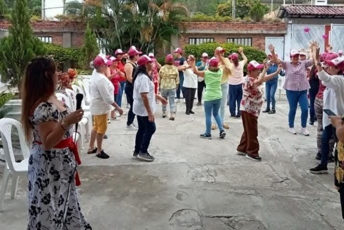 Un grupo de personas con sombreros rosas hace ejercicio al aire libre con los brazos en alto