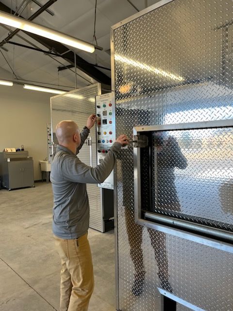 Man adjusting controls on industrial silver machine with open door.