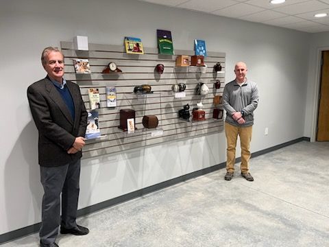 Two men standing by a wall display of urns. The room is modern with neutral colors.