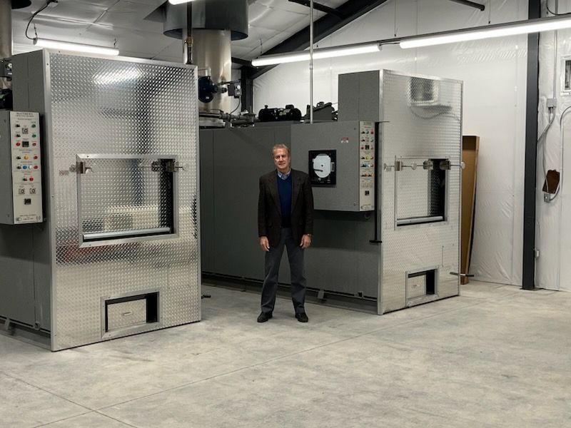 Man standing between two industrial crematoriums in a bright facility.