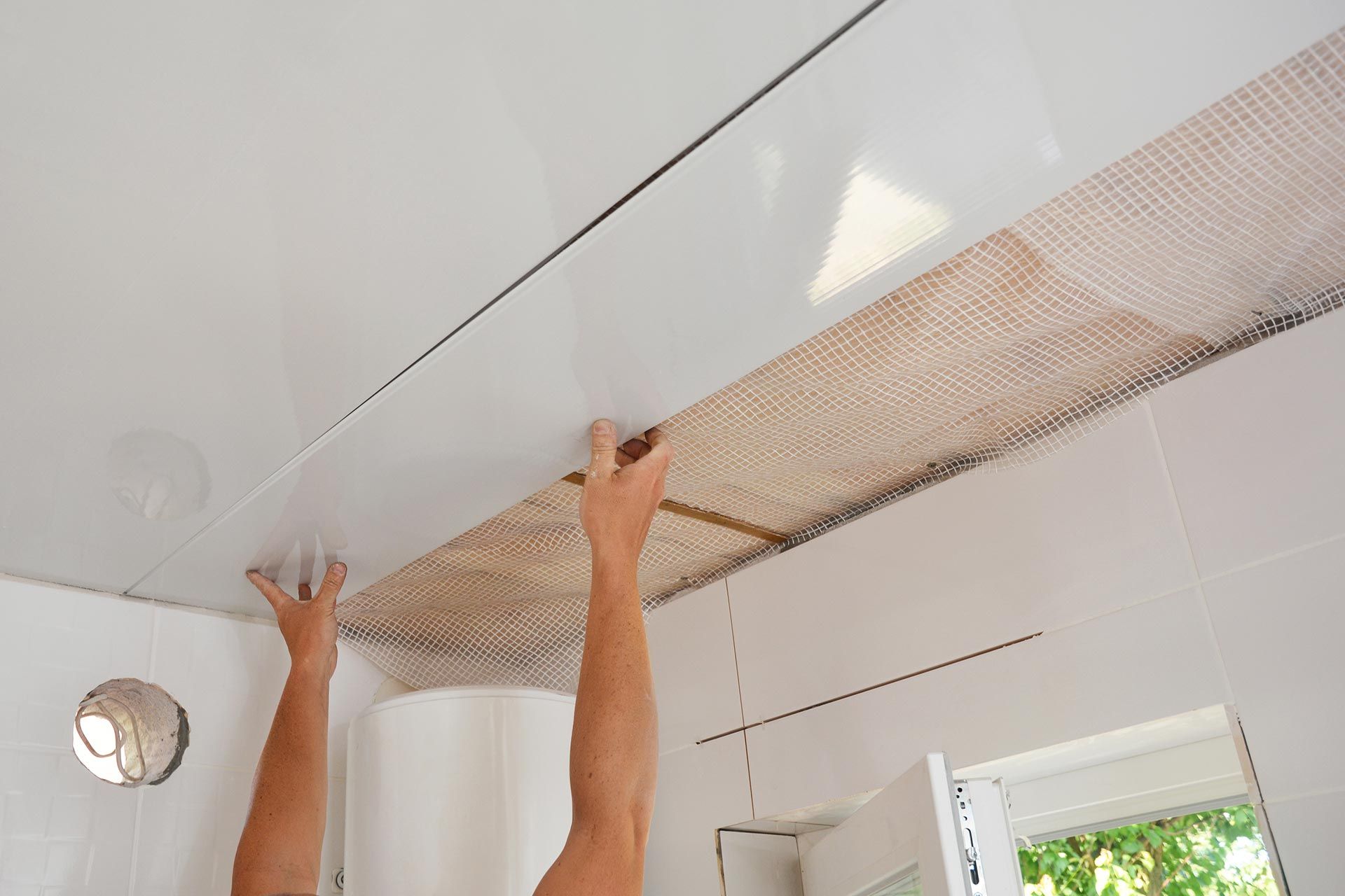 Technician fitting ceiling cladding sheets during indoor renovation and construction work.