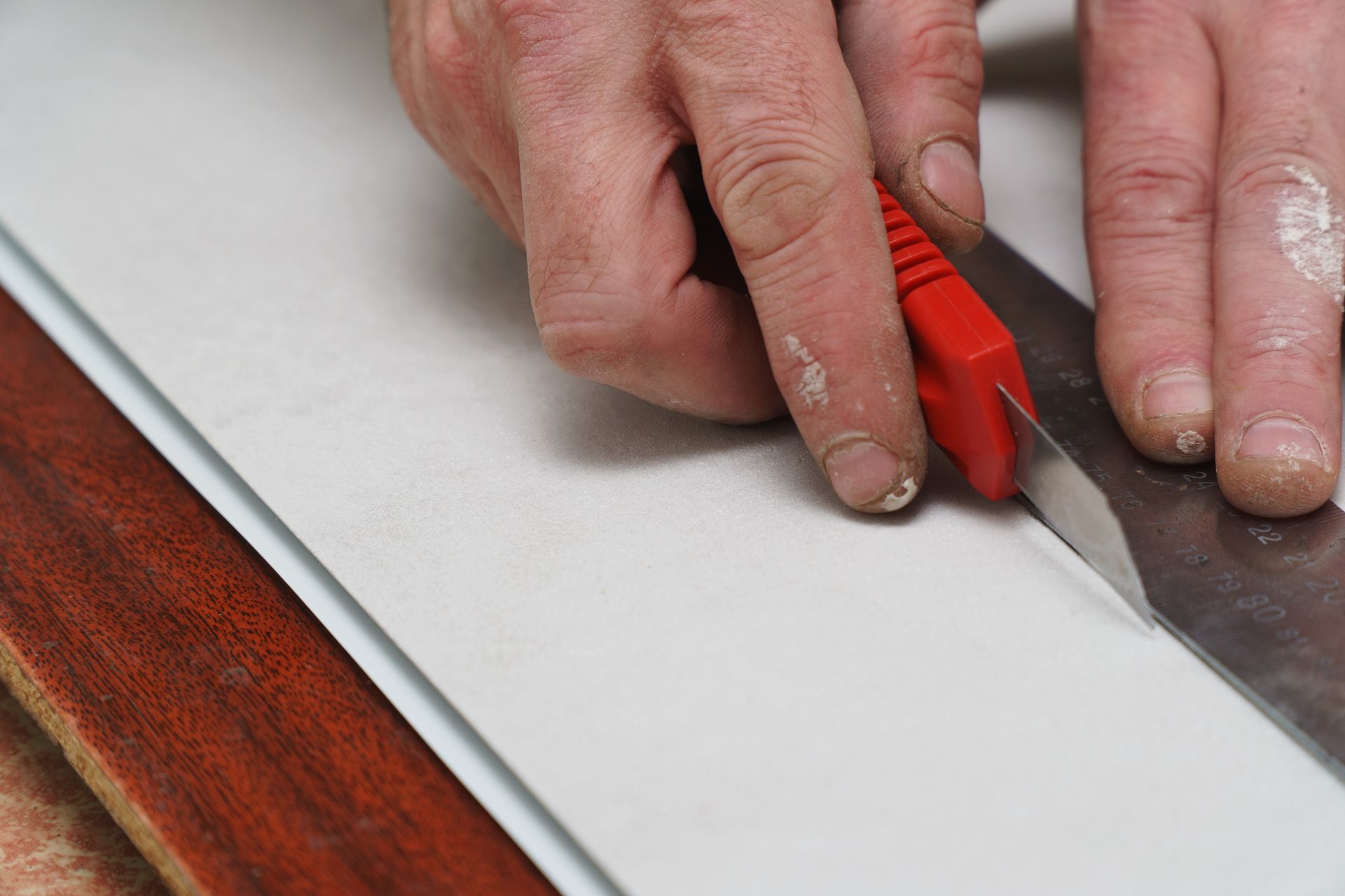 A close-up of a man’s hand cutting a plastic PVC panel with a construction knife.