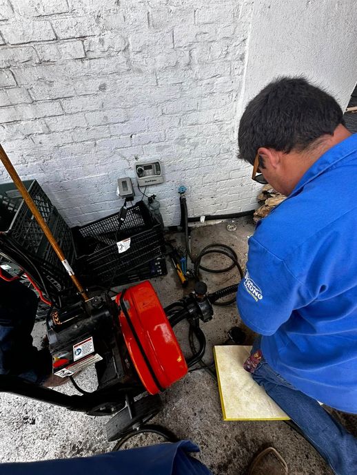 Person in blue jacket working on a red and black machine in a workshop corner