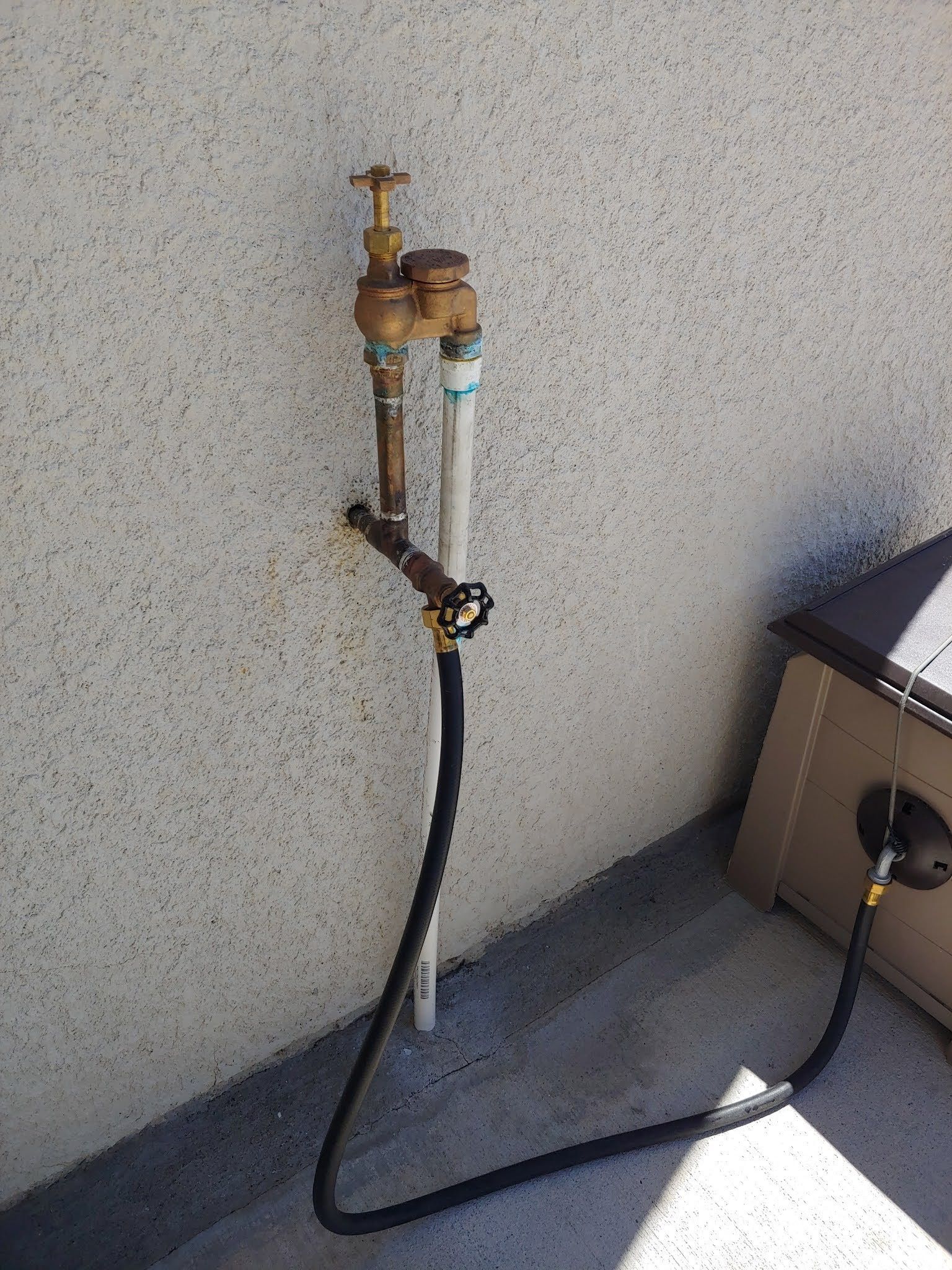 Gas hose and shutoff valves mounted on an exterior wall beside an HVAC unit.