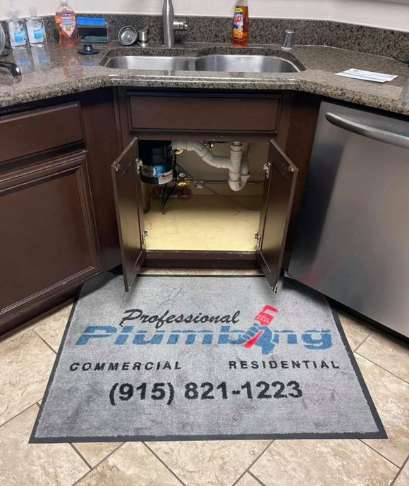 Under-sink cabinet with open doors in a kitchen, showing plumbing and a drain mat for Professional Plumbing Industrial