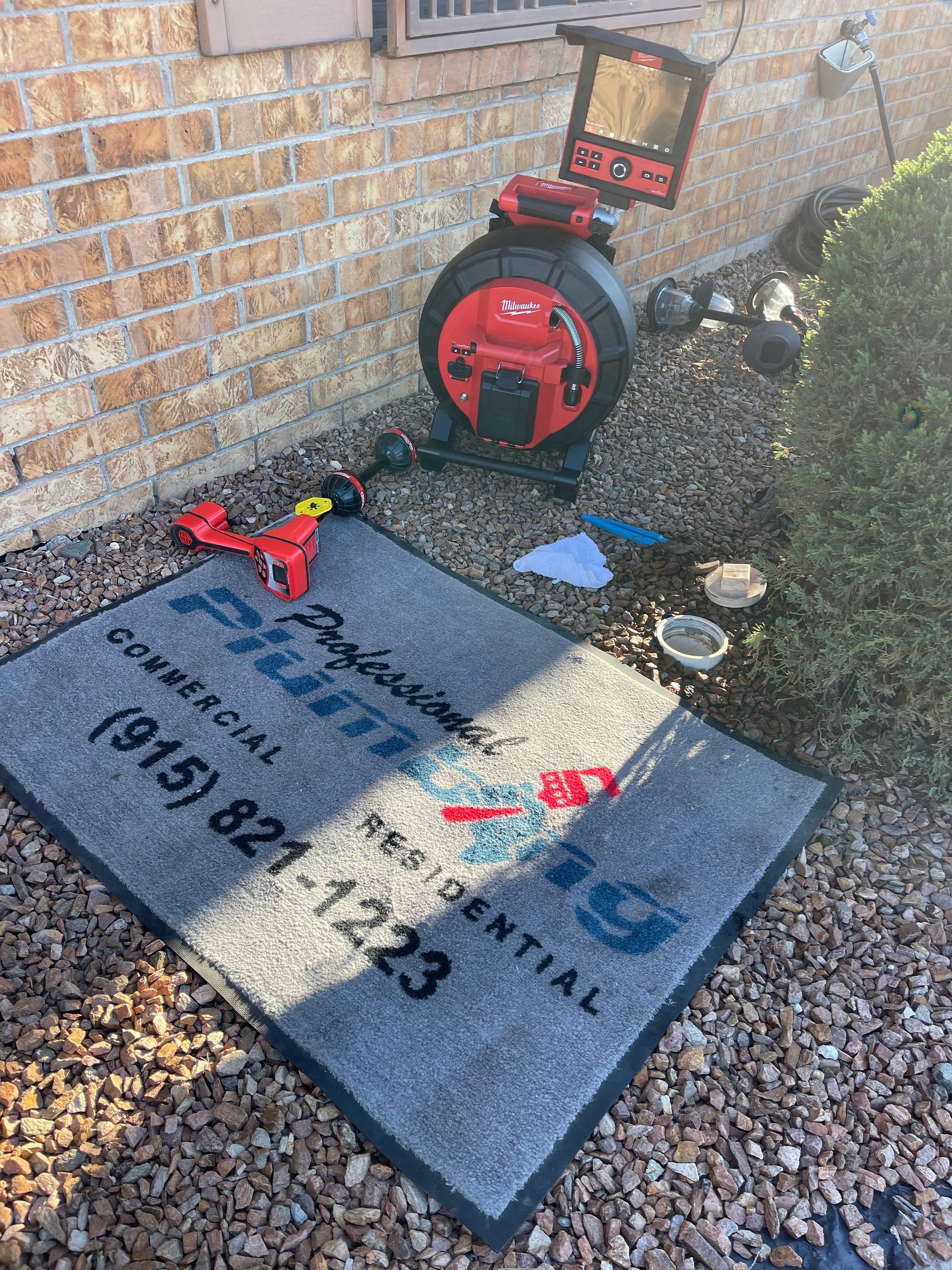 Service box and garden sign beside a brick wall, with a red tool and gravel path.