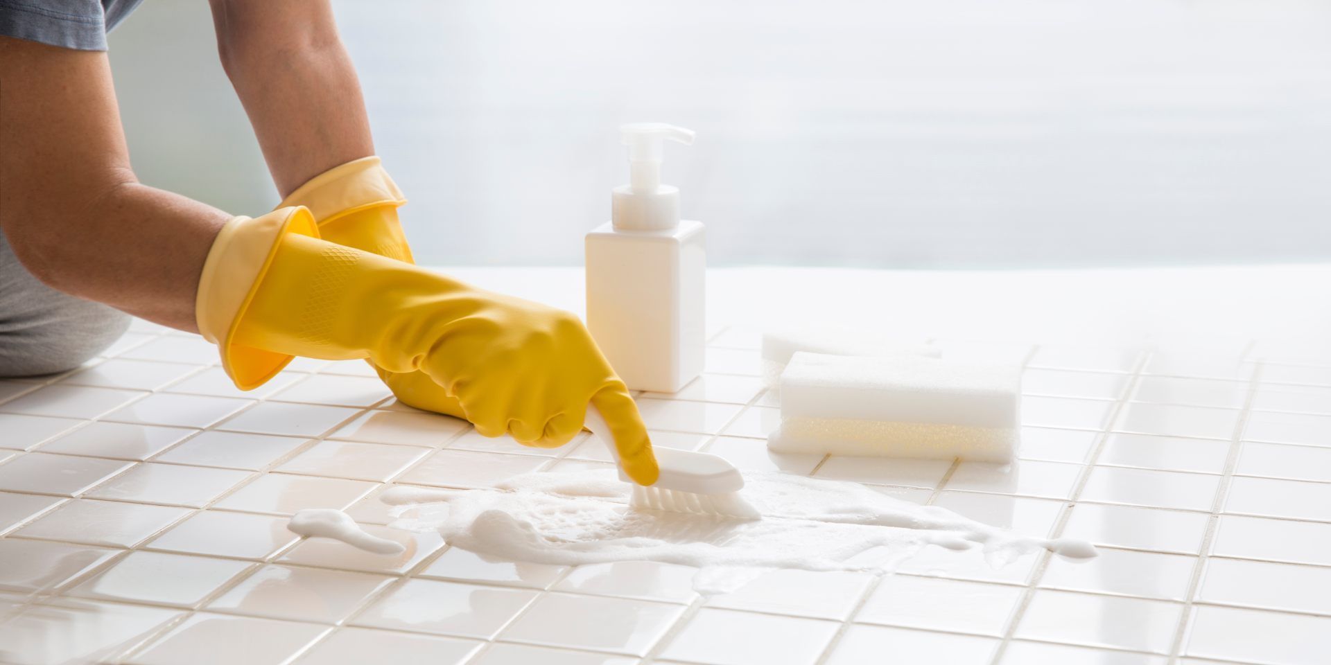 Gloved hands cleaning a tiled kitchen surface with a sponge and spray bottle