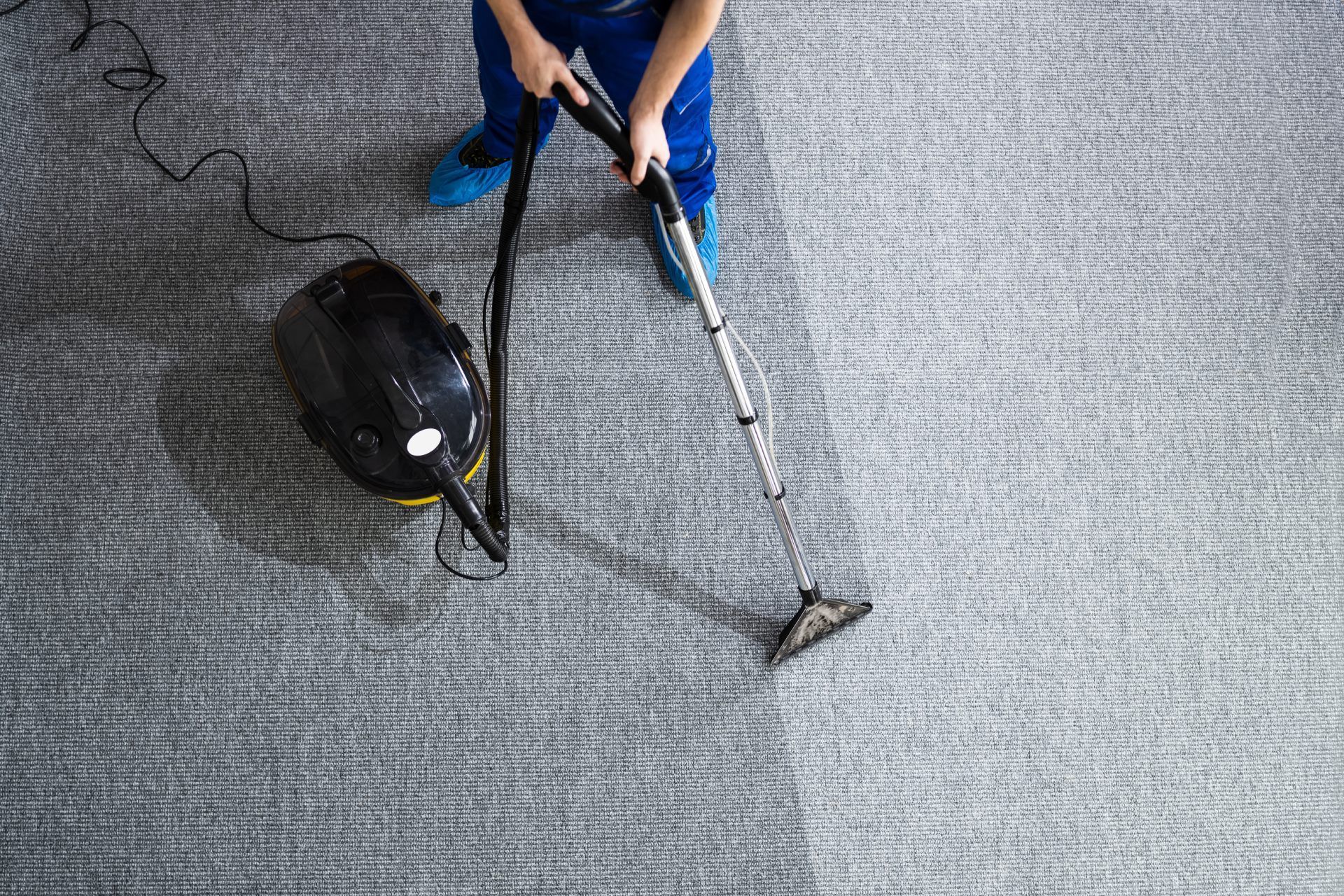 Person using a carpet cleaner on a gray carpet, viewed from above.