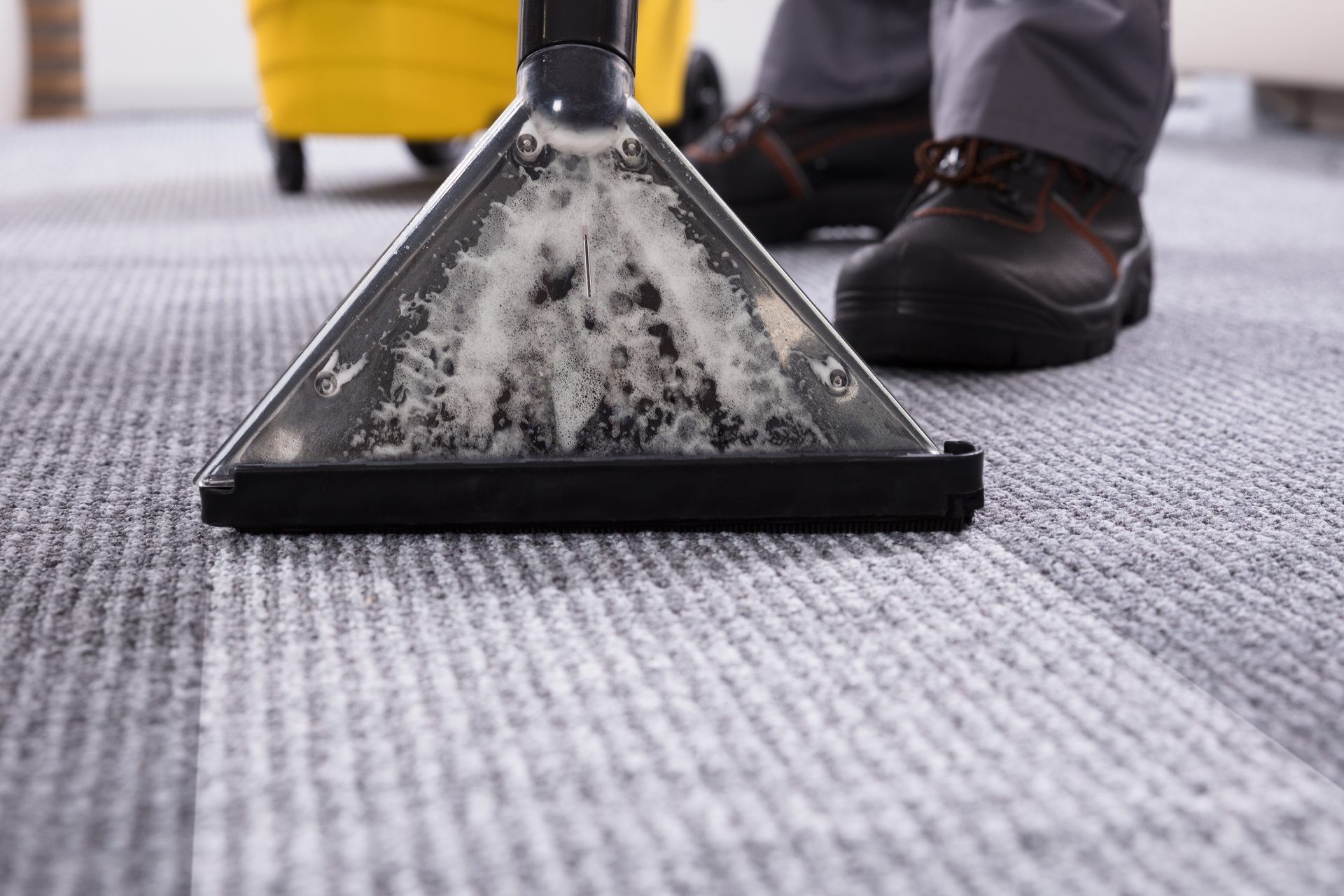 Carpet cleaner extracting dirt from a gray carpet beside a person’s shoes