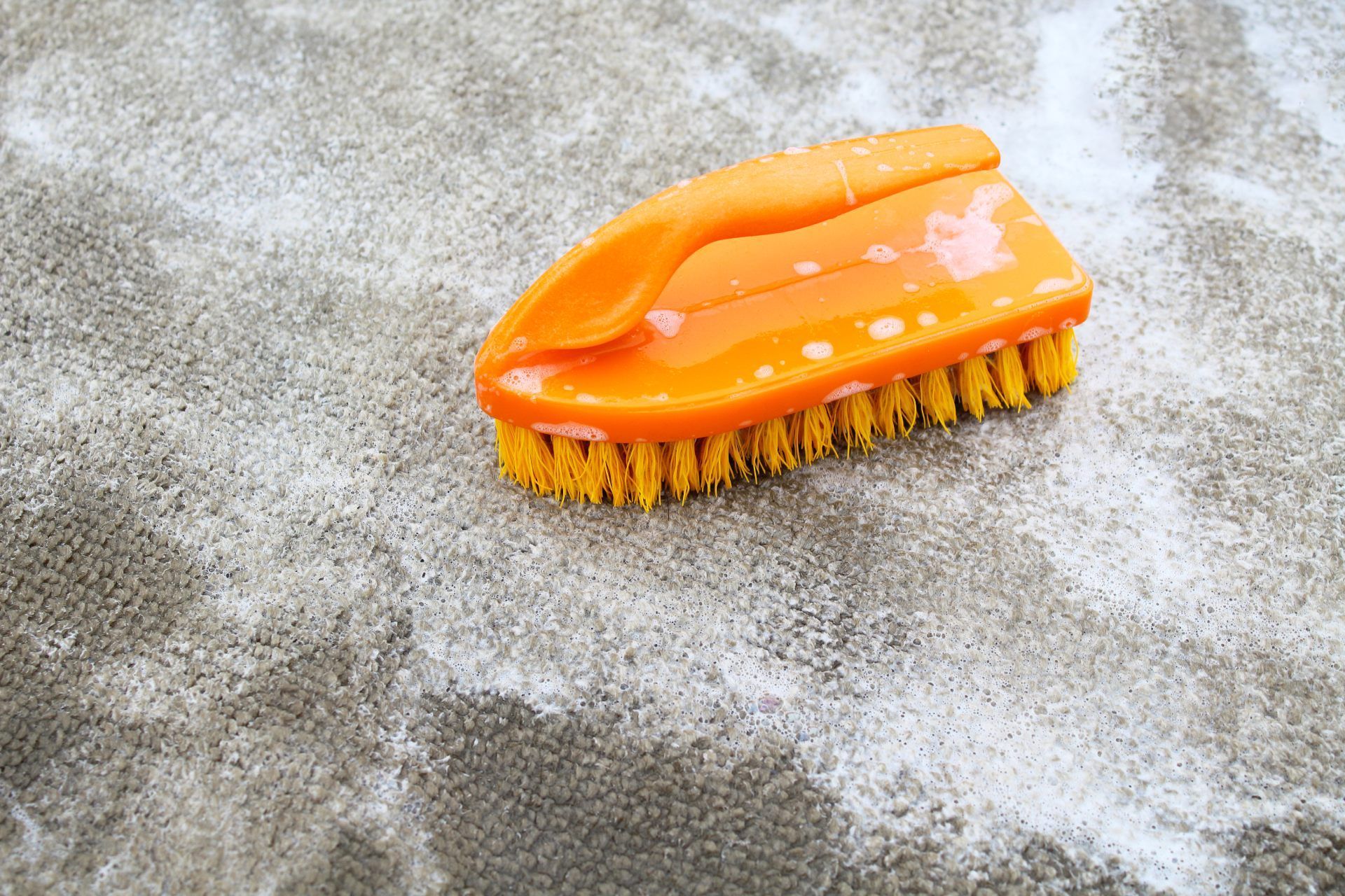 Orange scrub brush on a wet, soapy surface with foam around it