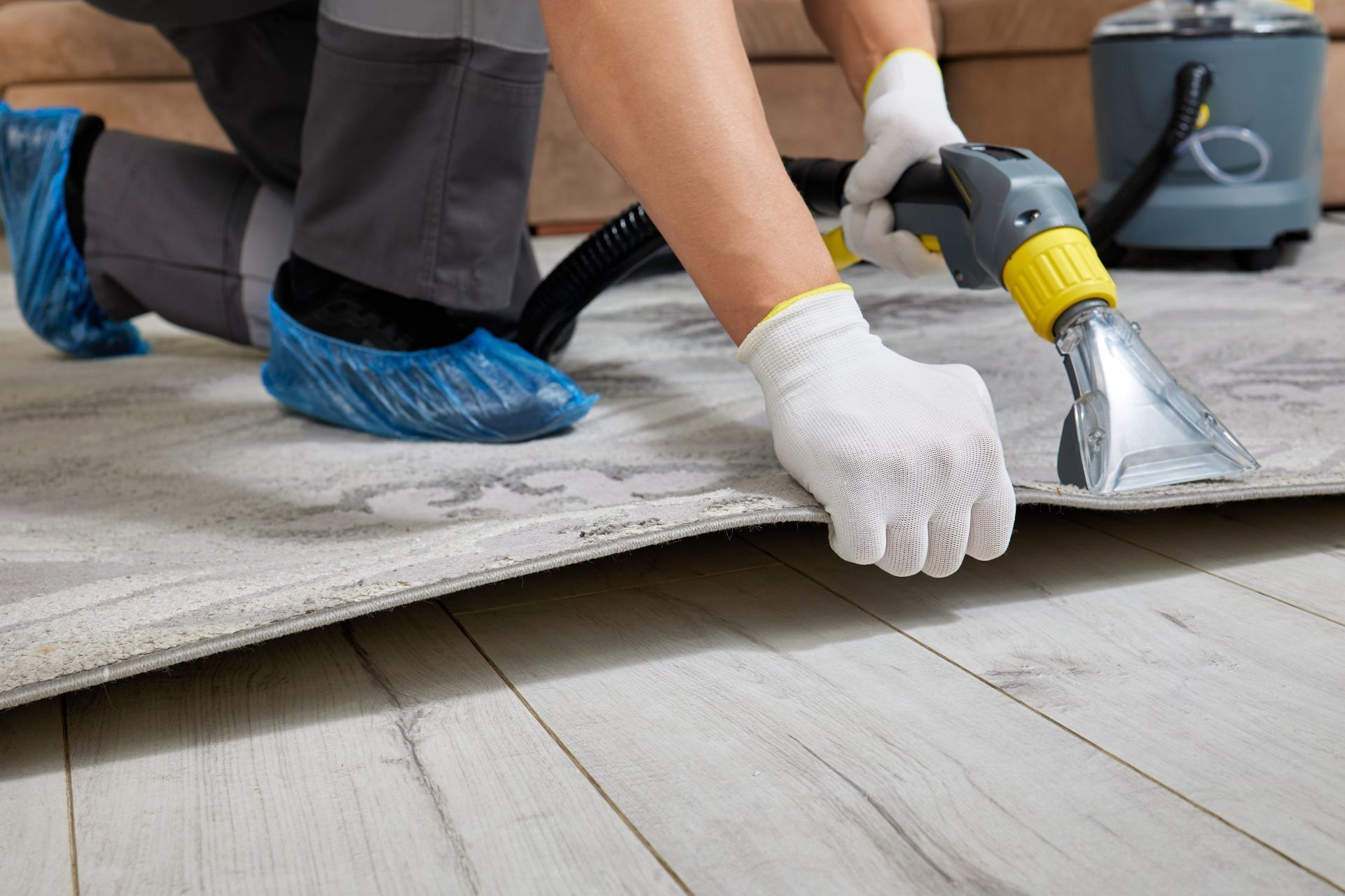 Worker vacuuming a dusty floor with a hose attachment and gloved hands while kneeling