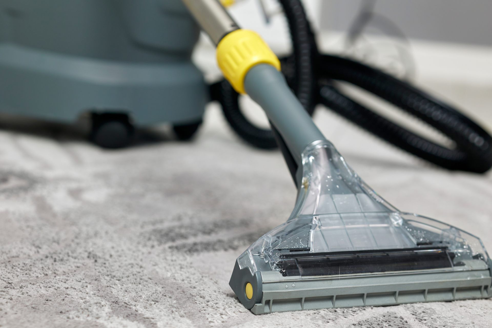 Steam cleaner vacuuming a gray carpet, removing dirt with a clear nozzle