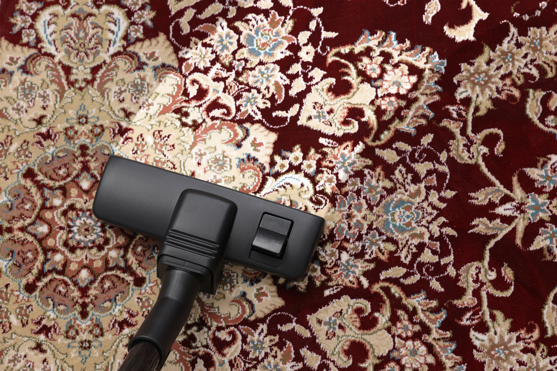 Black vacuum cleaner head on a red patterned rug