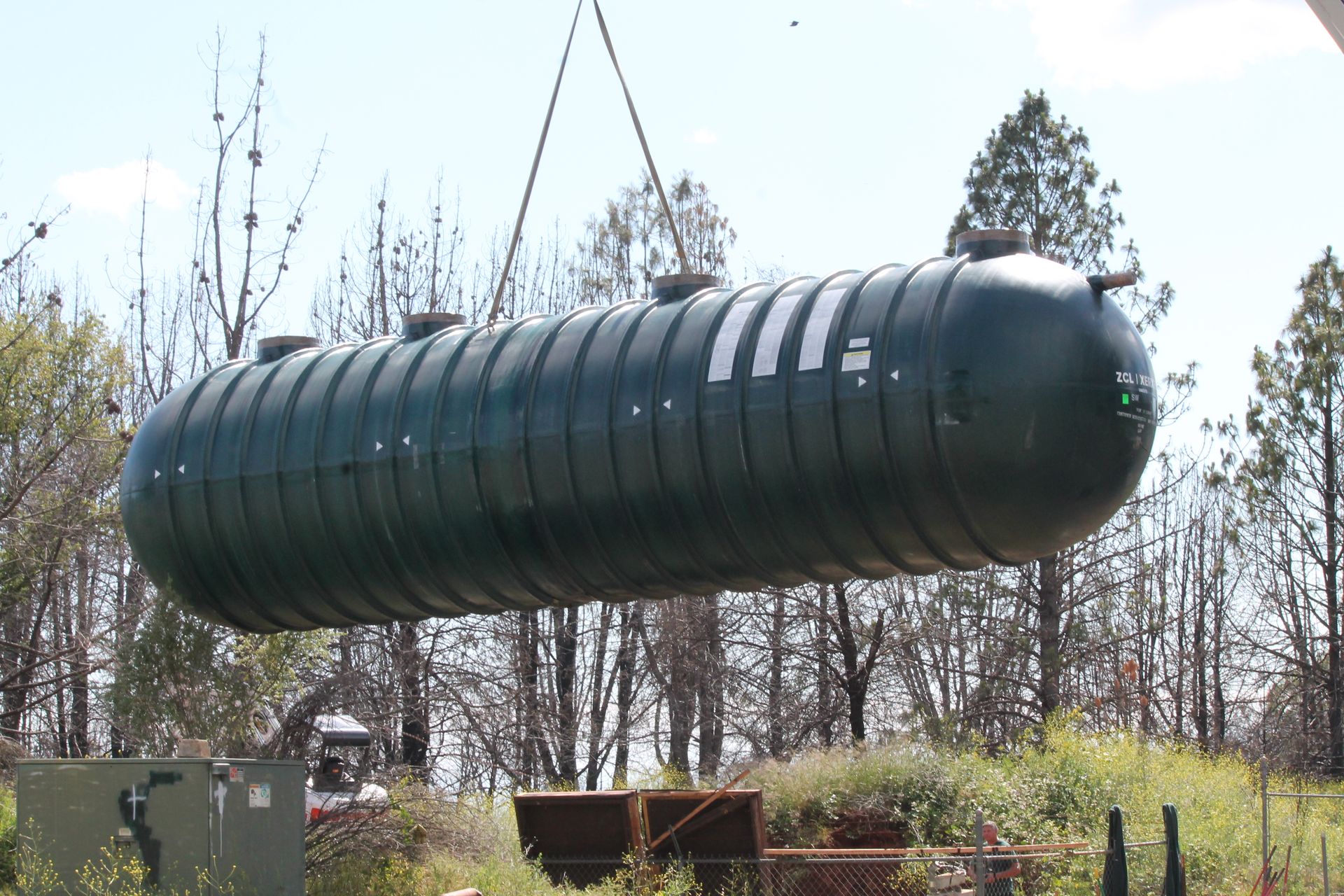 A large green tank is being lifted by a crane