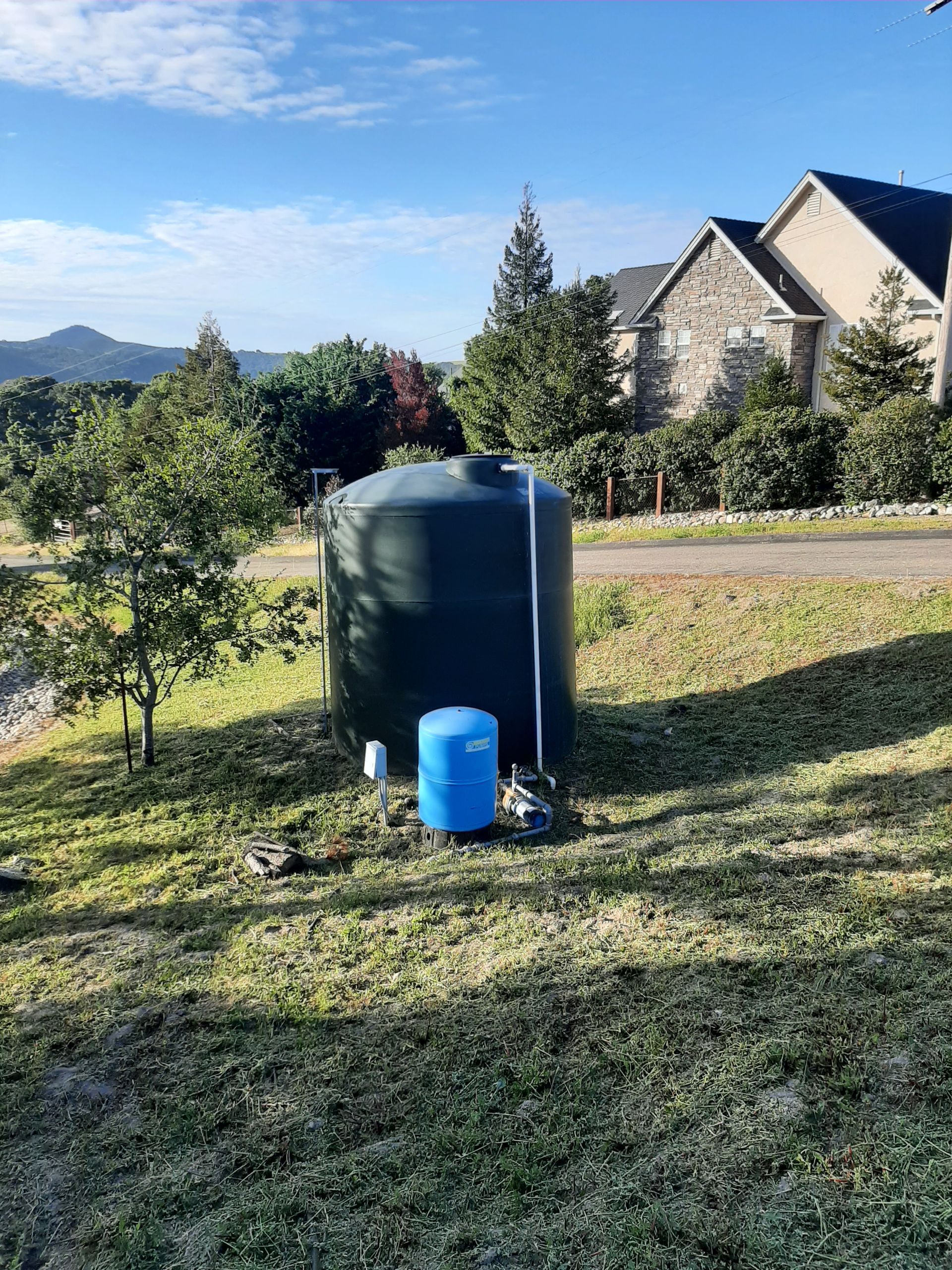 A water tank is sitting in the grass in front of a house.