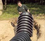 A man is standing next to a large black pipe in the dirt.