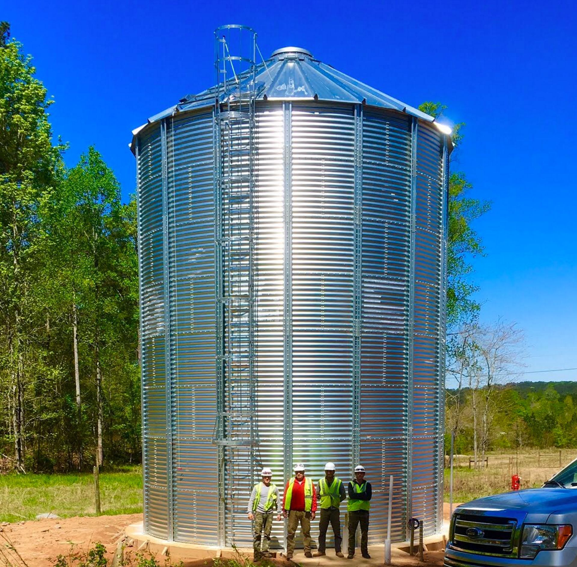 A group of men standing in front of a large metal silo