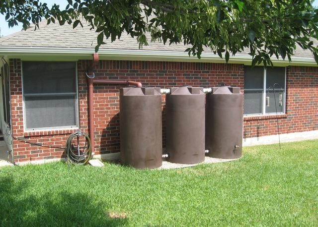 Three brown water tanks are in front of a brick house