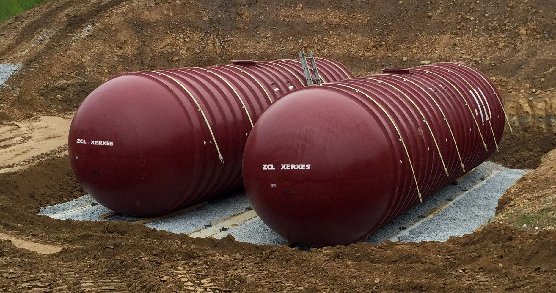 Two red tanks are sitting in the dirt in a field.