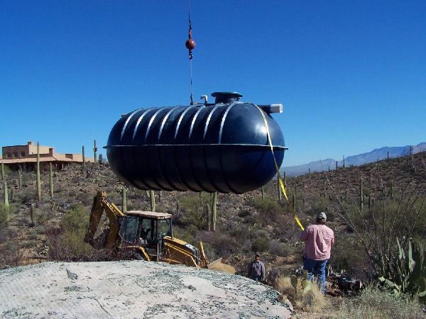 A large black tank is being lifted by a crane in the desert