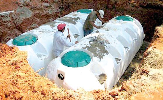 Two men are working on a large white tank in the dirt.
