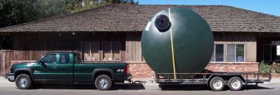 A green truck is pulling a large ball on a trailer