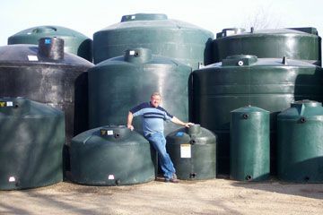 A man is standing in front of a stack of green water tanks.