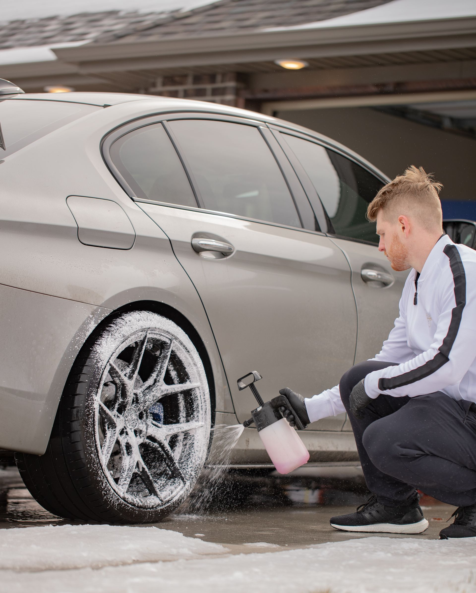 Man spraying soapy foam on a car wheel outdoors.