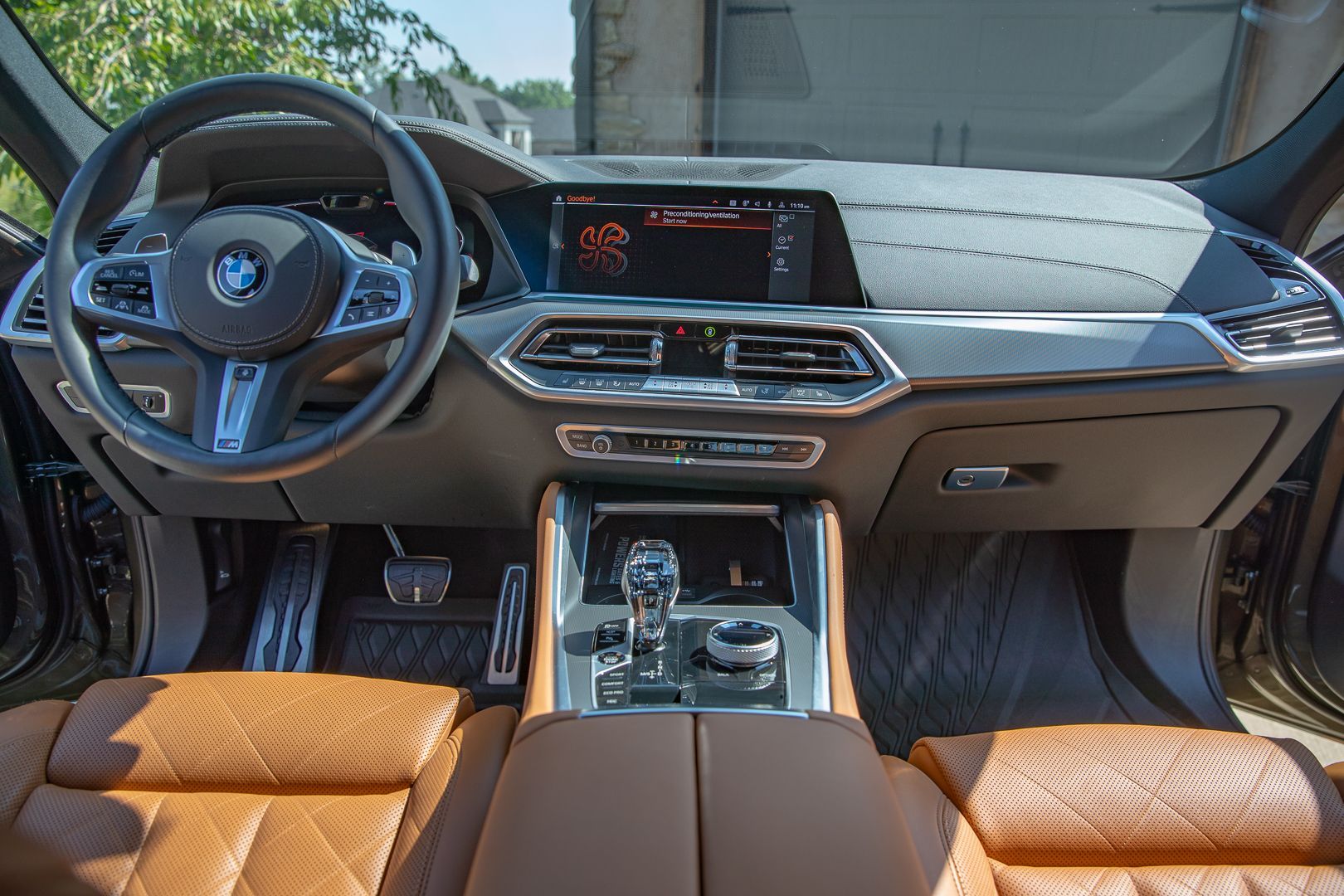 BMW car interior with tan leather seats, dashboard, steering wheel, and center console in daylight