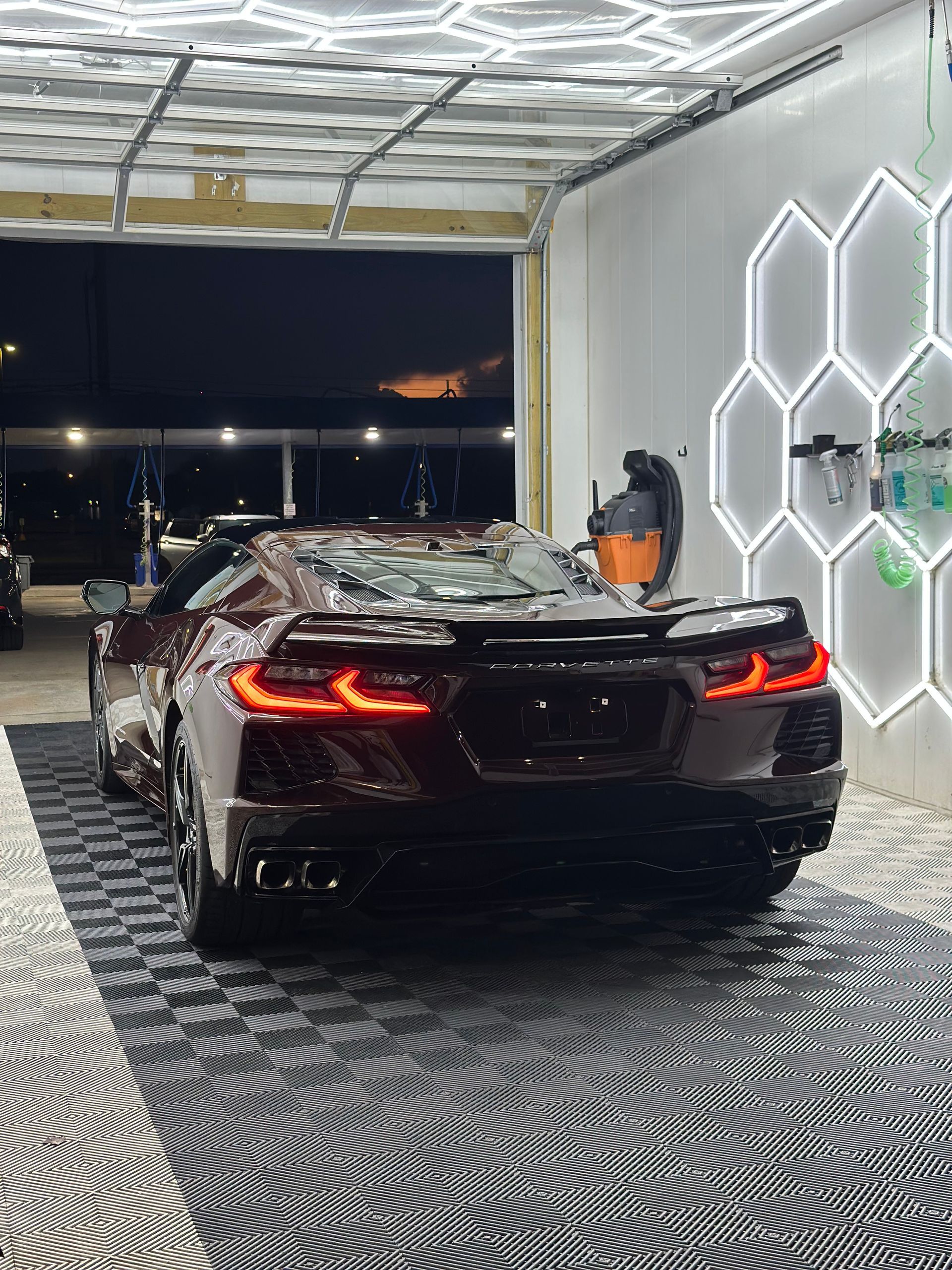 Black sports car in a garage at night, with a worker beside it and LED hexagon wall lights.