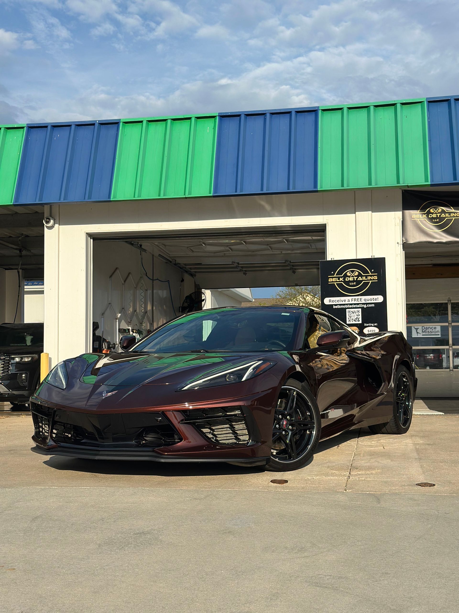 Dark maroon sports car parked outside a building with green and blue awnings