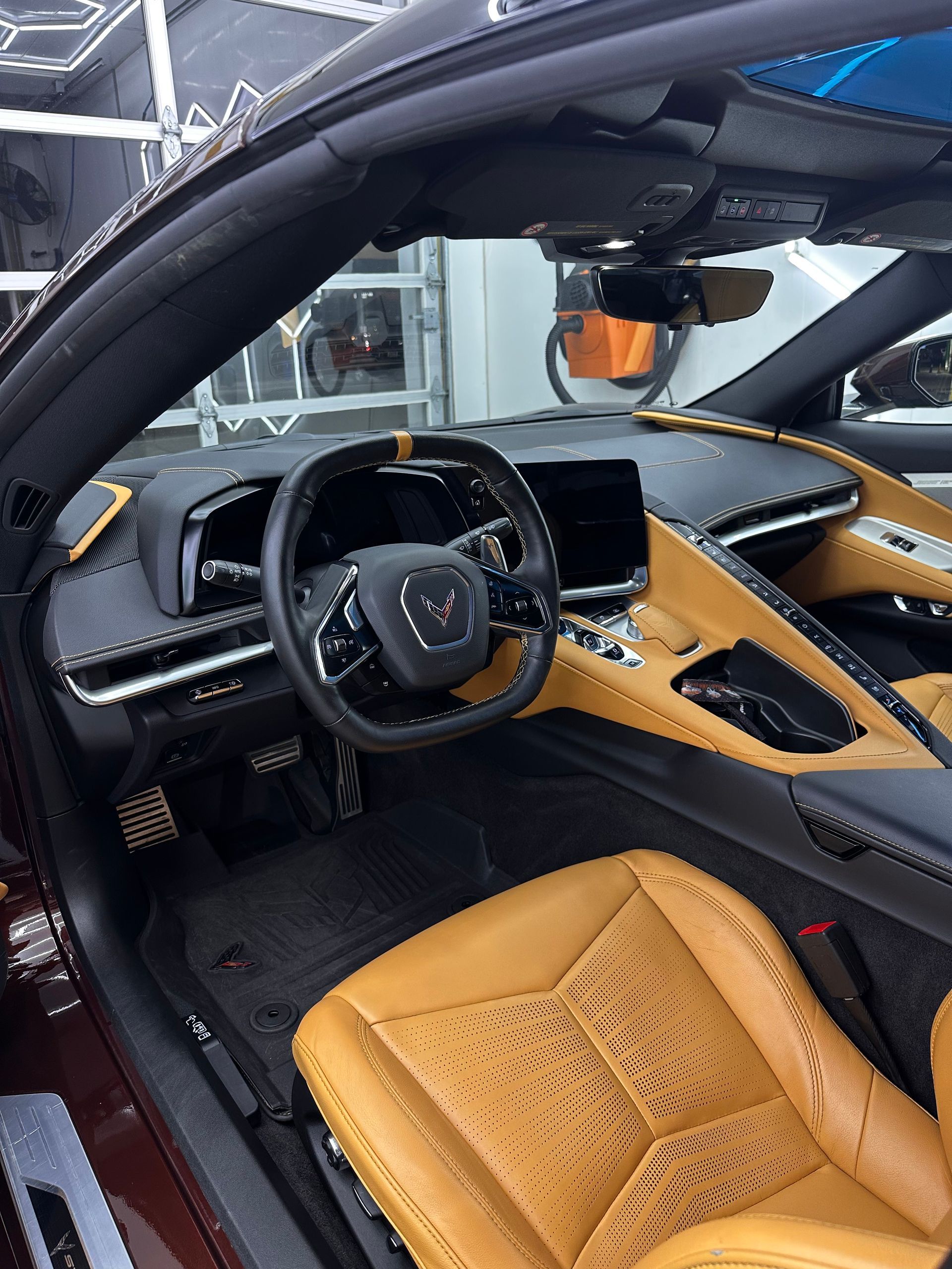 Luxury sports car interior with tan leather seats, black trim, and a digital dashboard visible through the open door.